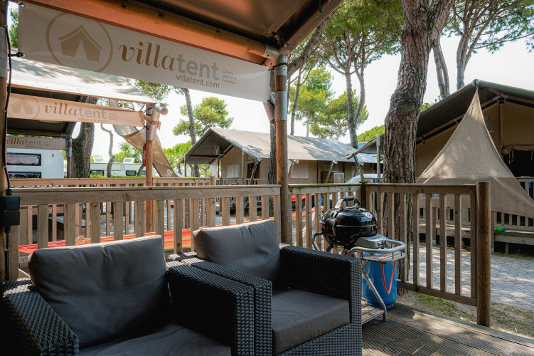 Outdoor seating area at Villatent Outback with rattan chairs, a grill, and multiple luxury safari tents nearby.