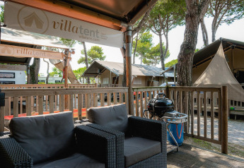 Terraza exterior en Villatent Outback con sillones de mimbre, barbacoa y tiendas safari de lujo alrededor.