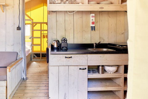Zona de cocina en una tienda safari llamada Villatent Outback, con estanterías y utensilios de madera.