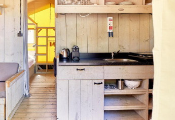 Kitchen area inside a safari tent called Villatent Outback with wooden shelves, sink, and utensils.