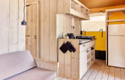 Interior of Villatent Outback safari tent featuring a small kitchen, fridge, shelves, and wooden sofa.