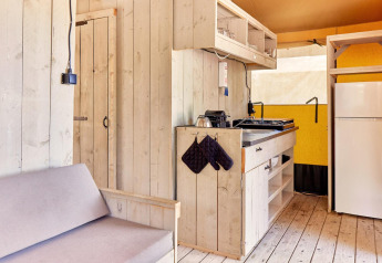 Interior of Villatent Outback safari tent featuring a small kitchen, fridge, shelves, and wooden sofa.