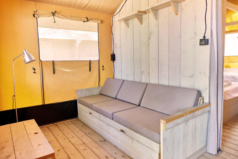 Interieurbeeld van een Villatent Outback safaritent met houten zetel, tafel en minimalistische inrichting.