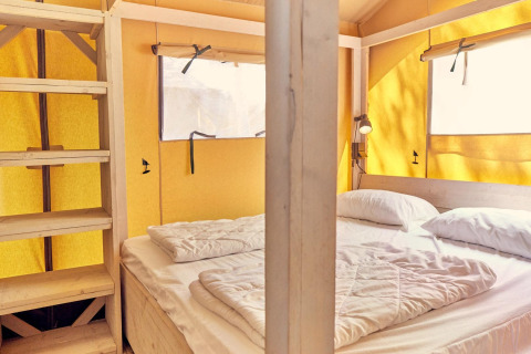 Vista interior de la tienda safari Villatent Outback con cama doble, estantería de madera y paredes amarillas.