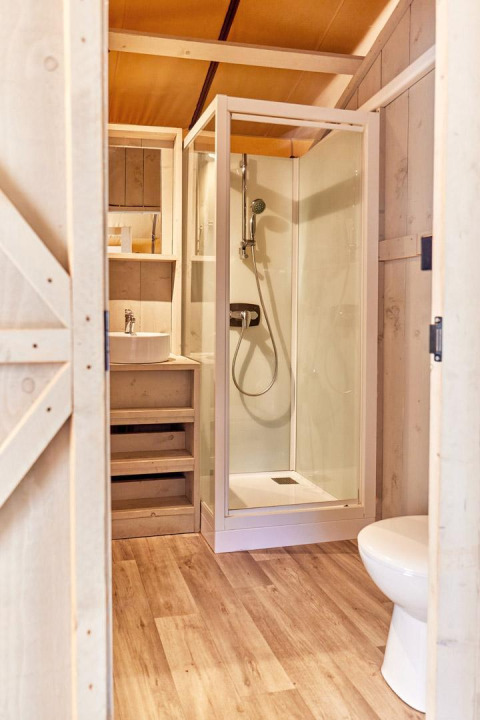 Baño moderno en una tienda safari con ducha, inodoro y lavabo sobre suelo de madera en Villatent Outback.
