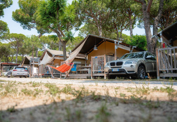 Tende safari in una zona alberata con auto parcheggiate e amaca al campeggio Villatent Outback.