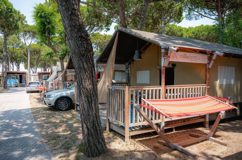 Tienda safari en Villatent Outback con hamaca y porche, rodeada de árboles altos y autos estacionados.