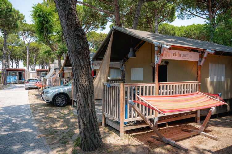 Safari tent at Villatent Outback with hammock and porch, surrounded by tall trees and parked cars.
