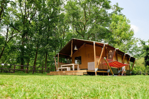 Safari-Zelt Villatent Nomad mit Veranda und Hängematte im Recreatiepark de Lucht, Niederlande, umgeben von Bäumen.