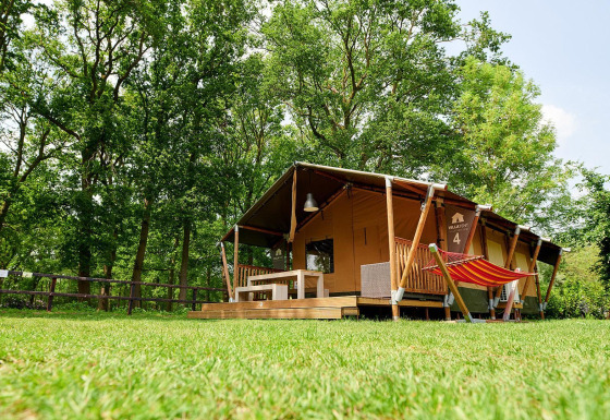 Safari-Zelt Villatent Nomad mit Veranda und Hängematte im Recreatiepark de Lucht, Niederlande, umgeben von Bäumen.