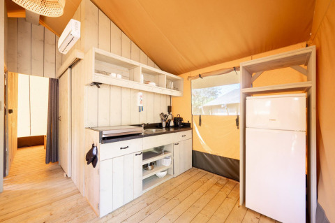 Cocina moderna dentro de una tienda safari Villatent Nomad con frigorífico, suelo de madera y estanterías.