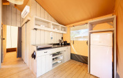 Moderne Küche im Safari-Zelt Villatent Nomad mit Holzfußboden, Kühlschrank und Wandregalen.