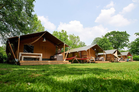 Safari tents at Recreatiepark de Lucht, Netherlands, with porches and hammocks in a green setting.