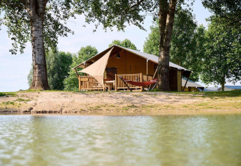Tienda safari Villatent Nomad en Camping Betuwe, Países Bajos, junto a un lago y rodeada de árboles.