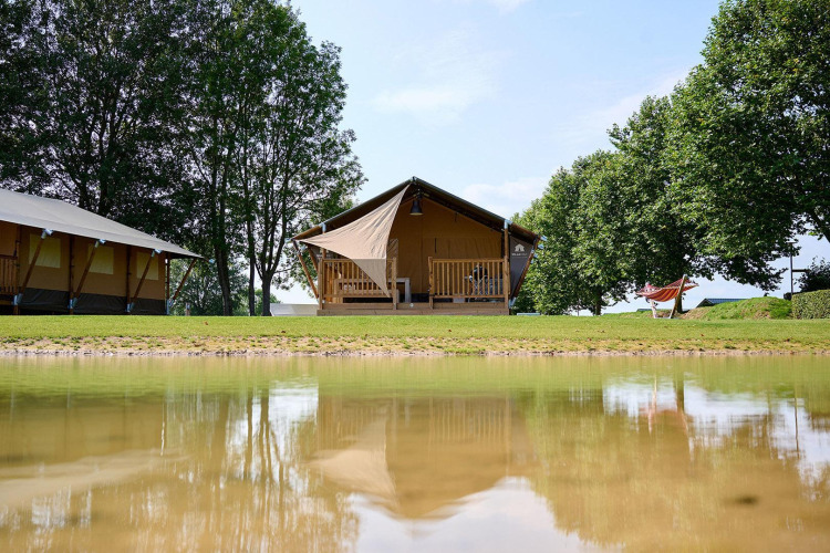 Safari tent Villatent Nomad at Camping Betuwe in the Netherlands, with lake reflection and lush trees.