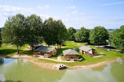 Tiendas safari junto al lago rodeadas de árboles verdes en Camping Betuwe, Países Bajos, perfectas para glamping.