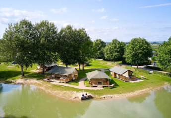 Tende safari sulle rive di un lago circondate da alberi verdi al Camping Betuwe, Paesi Bassi, ideale per glamping.