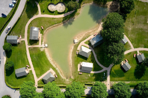 Vista aerea delle tende safari e dello stagno al Camping Betuwe nei Paesi Bassi, circondati dal verde.