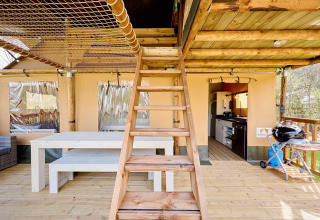 Interior de tienda safari Villatent Ranger con escaleras de madera, mesa de comedor y área de cocina abierta.