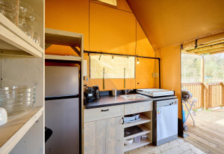 Gezellige keuken in een Villatent Ranger safaritent met moderne apparaten en zicht op een houten terras.