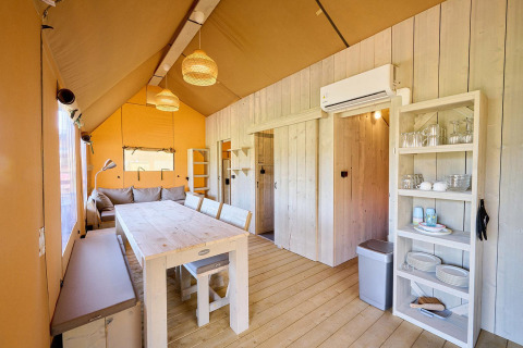 Binnenzicht van een Villatent Ranger safaritent met eettafel, sofa, open kast en airconditioning.