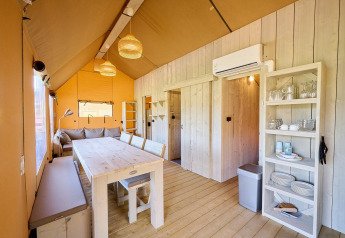 Interior view of a Villatent Ranger safari tent showing dining table, sofa, shelves with dishes, and air conditioning.