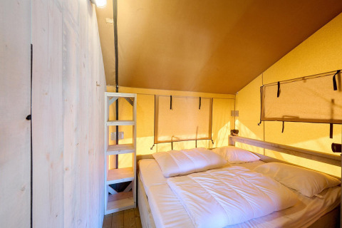 Interior de la tienda safari Villatent Ranger con cama doble, estantes de madera y paredes amarillas.