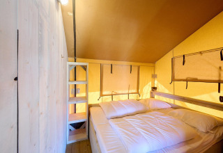 Interior de la tienda safari Villatent Ranger con cama doble, estantes de madera y paredes amarillas.