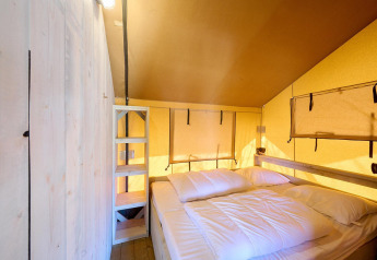 Innenraum des Safari-Zeltes Villatent Ranger mit Doppelbett, Holzregal und gelben Wänden.