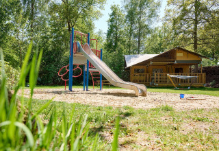 Parque infantil con tobogán y arenero frente a una tienda safari Villatent Ranger en Recreatiepark de Lucht.