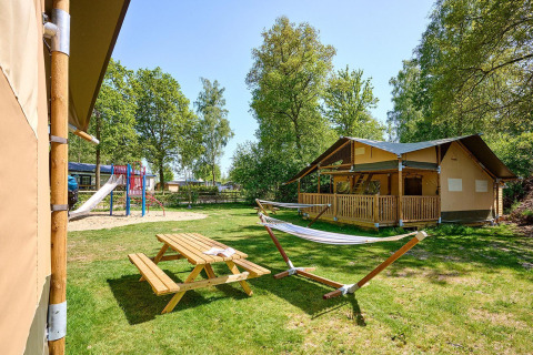 Tienda safari Villatent Ranger con área de juegos, mesa de picnic y hamaca en Recreatiepark de Lucht.