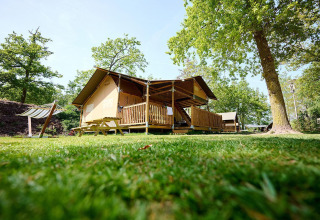 Tienda safari Villatent Ranger con porche de madera en Recreatiepark de Lucht, Países Bajos, rodeada de árboles.