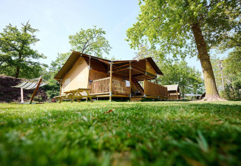 Safari-Zelt Villatent Ranger mit Holzveranda im Recreatiepark de Lucht, Niederlande, umgeben von Bäumen.