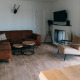 Living room in Veluwe Villa with brown sectional sofa, TV, modern armchair, fireplace, and wood flooring.