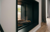Modern glass-enclosed fireplace in Veluwe Villa + sauna, displayed with wood logs and outdoor view reflected.