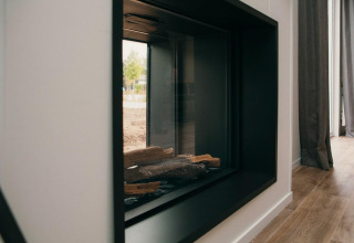 Modern glass-enclosed fireplace in Veluwe Villa + sauna, displayed with wood logs and outdoor view reflected.