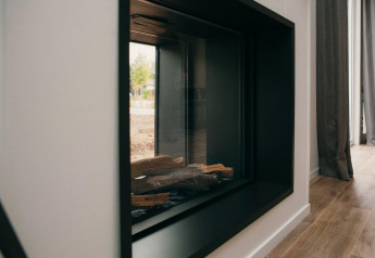 Moderne glazen haard in Veluwe Villa + sauna, met houtblokken en reflectie van het buitenzicht.