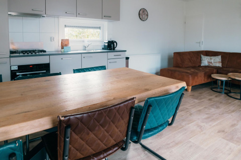 Moderne Küche und Wohnzimmer der Veluwe Villa + Sauna mit Holztisch, Stühlen und Ecksofa.