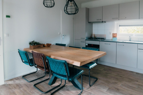 Comedor y cocina en Veluwe Villa + sauna con mesa de madera, sillas azules y decoración moderna.