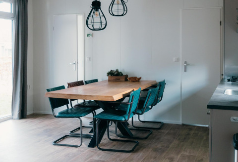 Comedor moderno en Veluwe Villa con mesa de madera, seis sillas azules, lámparas colgantes y luz natural.