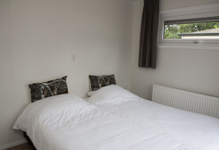 Soveværelse med to enkeltsenge, hvide dyner, ulve-puder og vindue på Veluwe Villa + sauna ved De Boshoek.