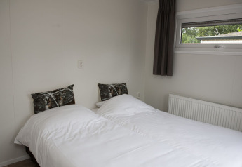 Soveværelse med to enkeltsenge, hvide dyner, ulve-puder og vindue på Veluwe Villa + sauna ved De Boshoek.