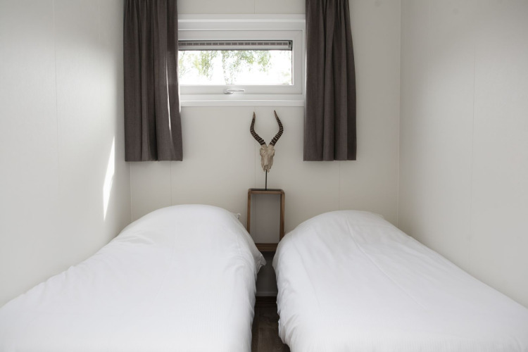 Dormitorio con dos camas individuales, ropa de cama blanca, ventana pequeña y cráneo de antílope en la pared.