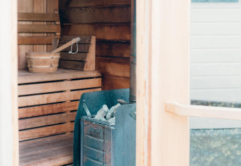 Interior view of a sauna at Veluwe Villa, showing wooden benches, a bucket, and a stove with stones.