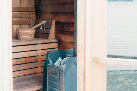 Interior view of a sauna at Veluwe Villa, showing wooden benches, a bucket, and a stove with stones.