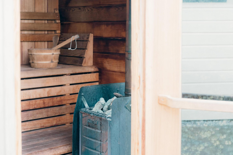 Vista interior de una sauna en Veluwe Villa con bancos de madera, un cubo y una estufa con piedras.