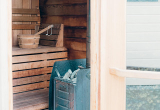 Vista interior de una sauna en Veluwe Villa con bancos de madera, un cubo y una estufa con piedras.