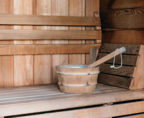 Wooden sauna interior at Veluwe Villa + sauna, showing a bench, bucket, and ladle for relaxation.