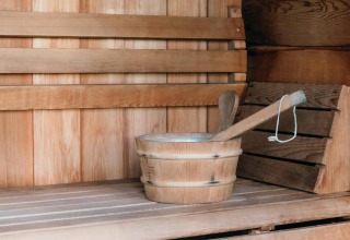 Wooden sauna interior at Veluwe Villa + sauna, showing a bench, bucket, and ladle for relaxation.