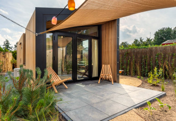 Modern tiny house at Holiday Park De IJsvogel in the Netherlands, with patio, wood siding and two chairs.
